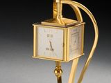 une image représentant une horloge dorée posée sur un socle, sur une surface grise