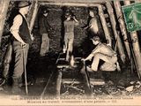 Plusieurs hommes travaillent dans une mine, avec un pilon posé par terre.