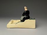 figurine of a woman sitting in a boat on a gray surface