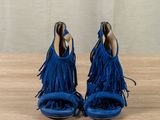 blue fringe sandals on a wooden table with a wall in the background