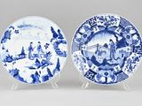 two blue and white plates with figures on them on stands