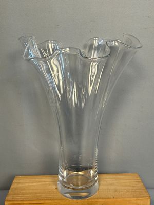 un vase en verre transparent posé sur un socle en bois, sur une table