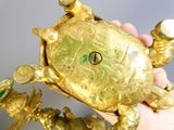 une main tenant une tortue en or dont la carapace renferme une perle