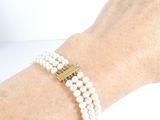 someone is wearing a bracelet with pearls and a gold cross on it