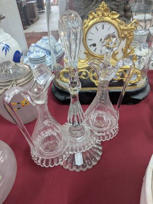 de nombreux objets en verre posés sur une table, avec une horloge en arrière-plan