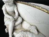 a statue of a boy sitting on a bed with a sheep