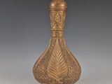 un vase ancien en laiton orné d'un motif décoratif, posé sur un socle