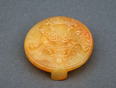 une image représentant un bouton en jade jaune sculpté orné d'un lion