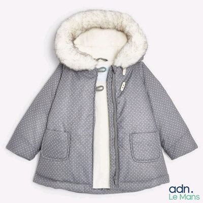 La veste est grise et blanche, avec une capuche et un col doublé de fourrure.