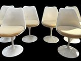 six white tulip chairs with beige cushions on a black background
