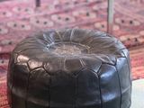 a black leather pouffe sitting on the floor in a living room