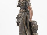 bronze statue of a woman with luggage on a pedestal