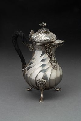 une cafetière ancienne en argent, avec une poignée noire sur un fond gris