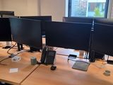 trois écrans d'ordinateur posés sur le bureau, avec un téléphone