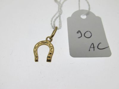 un gros plan sur un pendentif en forme de fer à cheval en or, sur lequel est accrochée une étiquette de prix