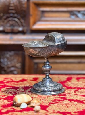 un bol en argent posé sur une nappe rouge, à côté de quelques noix