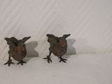 two small metal birds that are standing on a white surface