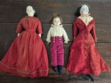 trois poupées anciennes représentant des femmes en robe rouge, couchées les unes à côté des autres