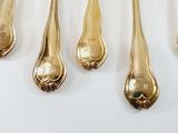 five gold spoons and a fork on a white surface