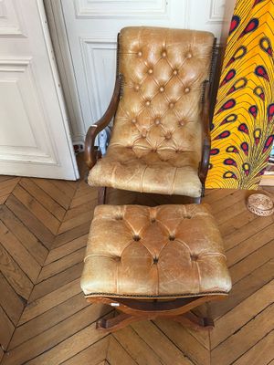 fauteuil et repose-pieds en cuir marron dans une pièce aux murs recouverts d'un papier peint à motifs de paons