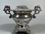 an antique silverplated teapot with ornate handles on a stand