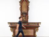 un homme passant devant une grande horloge en bois dans une pièce