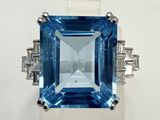 une photo d'une bague en topaze bleue et diamants posée sur une surface blanche