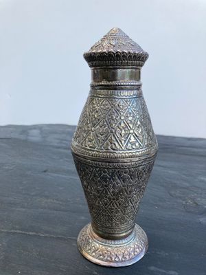 un vase en argent posé sur une table, avec un mur blanc en arrière-plan