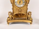 a gold clock sitting on top of a table next to a pair of candles