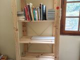 une étagère en bois avec des livres posés dessus, dans un coin de la pièce