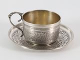une tasse et une soucoupe anciennes en argent, posées sur une soucoupe, sur un fond blanc