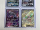 quatre cartes Pokémon différentes dans des pochettes en plastique, posées sur une surface blanche