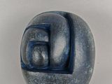 une sculpture représentant un visage, de couleur bleue et blanche, posée sur une surface blanche