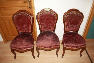 three red velvet chairs sitting next to each other on a wooden floor