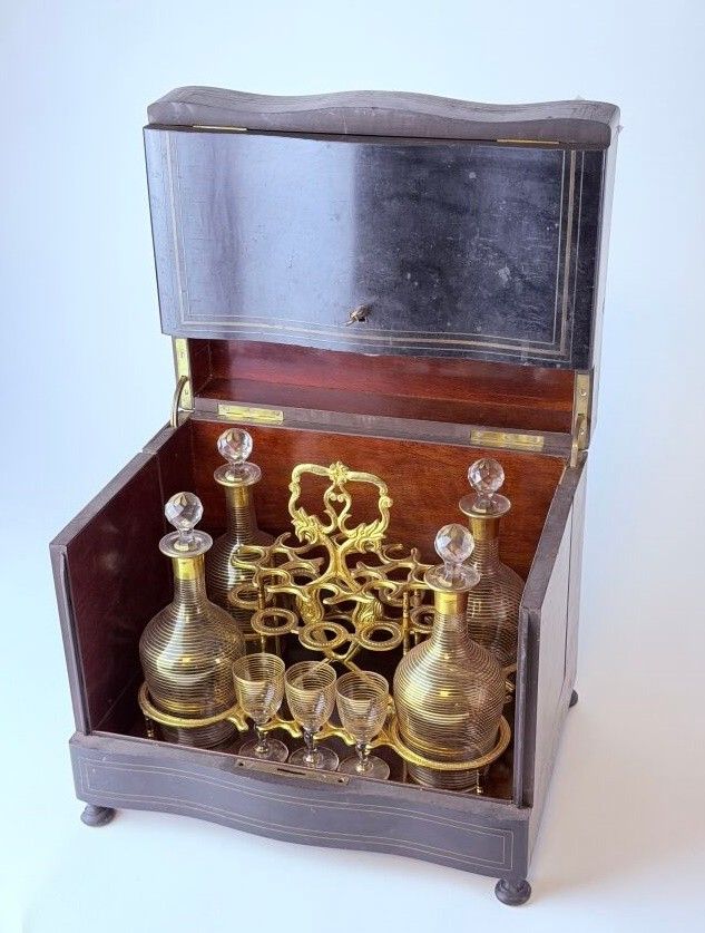 Cave à liqueur quadripode en bois à décor de filets et d'un cartouche en laiton. Flaconnage en cristal translucide et...
