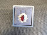 bague en argent avec une pierre rouge entourée de perles, posée sur une table