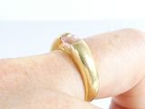 a person holding a gold ring with a pink stone on it