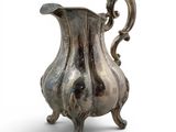 an old silver pitcher sitting on a stand on a white surface