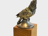 un oiseau en bronze posé sur un bloc de bois