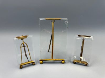 trois meubles en verre et en laiton posés sur une surface blanche