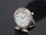 une petite horloge argentée posée sur une surface noire