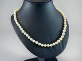 a white pearl necklace on a black mannequin stand