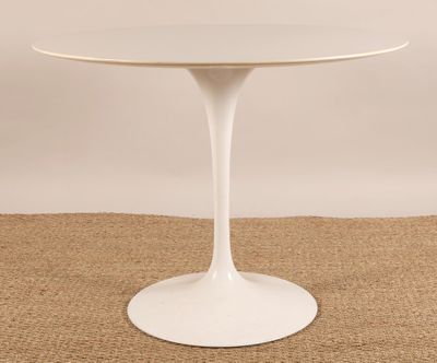 une table blanche avec un piètement rond, posée sur un sol recouvert de moquette