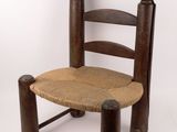 chaise en bois avec assise et dossier en corde, adossée à un mur blanc