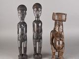 deux figurines en bois représentant un homme et une femme portant un panier sur la tête