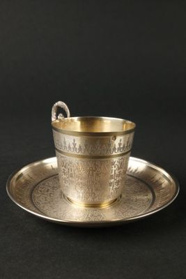 une tasse et une soucoupe argentées posées sur une soucoupe, sur un fond noir