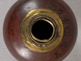 a brown vase with a gold rim sitting on a white surface