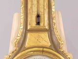 une horloge dorée posée sur un socle en bois, sur fond gris