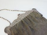 un sac à main ancien en maille d'argent, muni d'une bandoulière en chaîne, posé sur une surface blanche