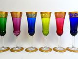 six different colored wine glasses lined up in a row on a white surface